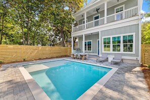 A two-story house with a swimming pool, a wooden fence, and a patio with outdoor furniture.