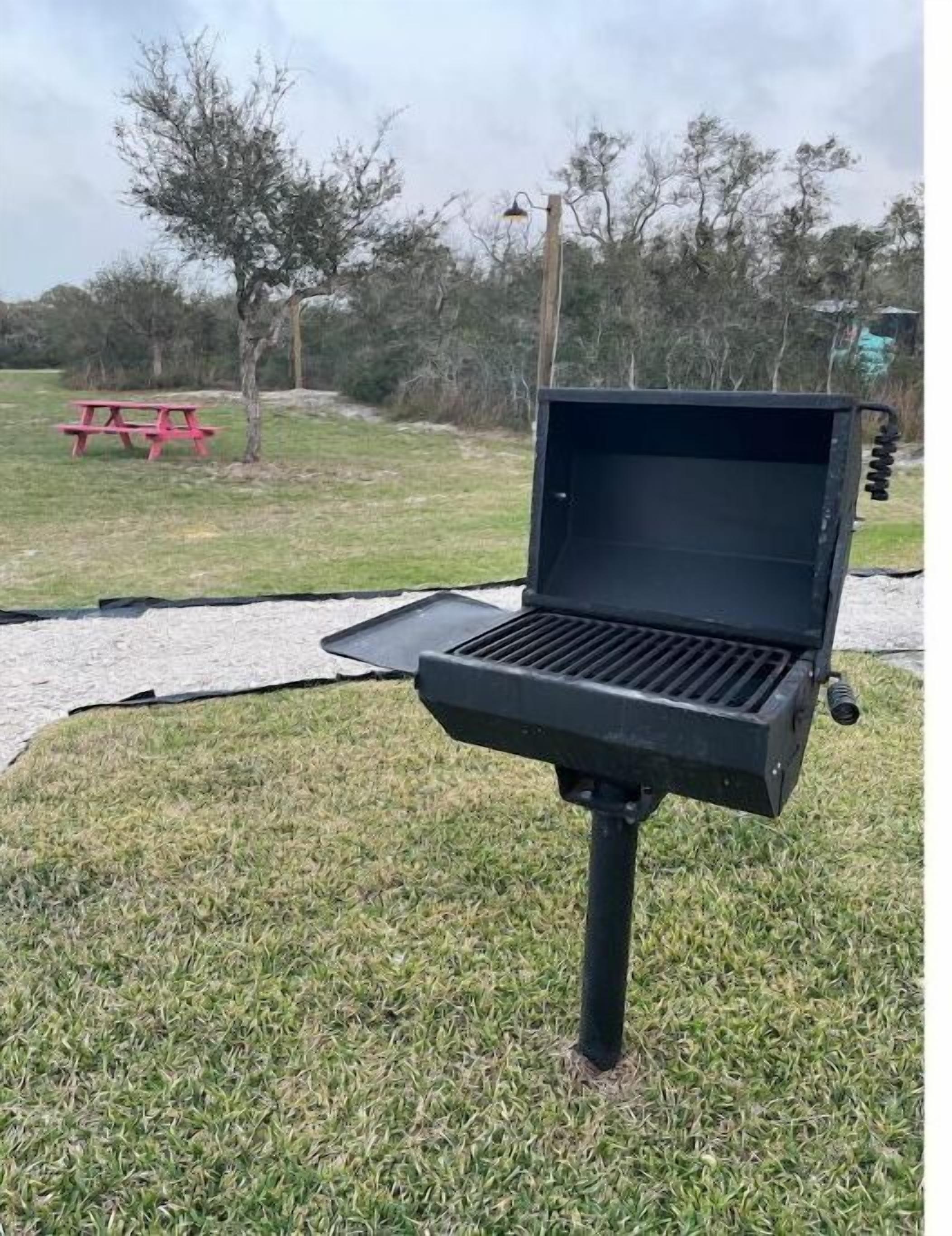 Ein tragbarer Grill auf einer Rasenfläche mit einem Picknicktisch und Bäumen im Hintergrund.