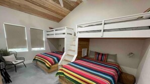 A bedroom with bunk beds, a chair, and a window.