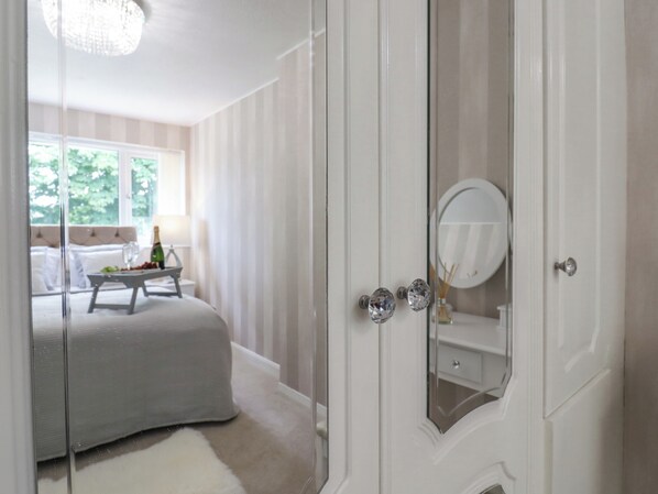 A bedroom with a bed, a bedside table with a bottle, and a mirror on the door.