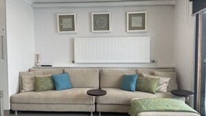 A living room with a sofa, two side tables, and a radiator. There are three framed pictures on the wall. - Adorable 2 Bedroom Ski Chalet (Hotham Heights)