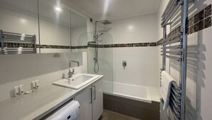 A modern bathroom with a glass-enclosed shower, a white sink, a built-in washing machine, and a bathtub with a towel rack. - Adorable 2 Bedroom Ski Chalet (Hotham Heights)