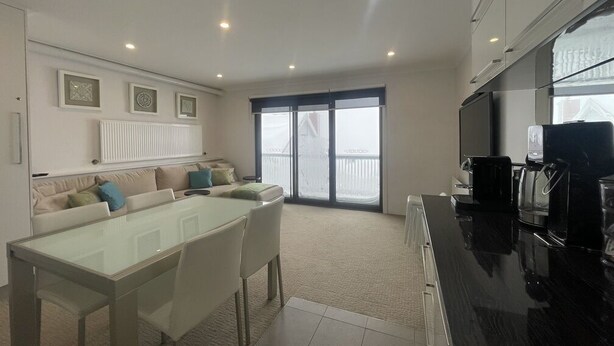 A modern kitchen with a dining area, a large window, and a built-in oven. - Adorable 2 Bedroom Ski Chalet (Hotham Heights)