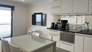 A modern kitchen with white cabinets, a black countertop, and stainless steel appliances. There is a dining table with chairs and a flat-screen TV mounted above it. - Adorable 2 Bedroom Ski Chalet (Hotham Heights)