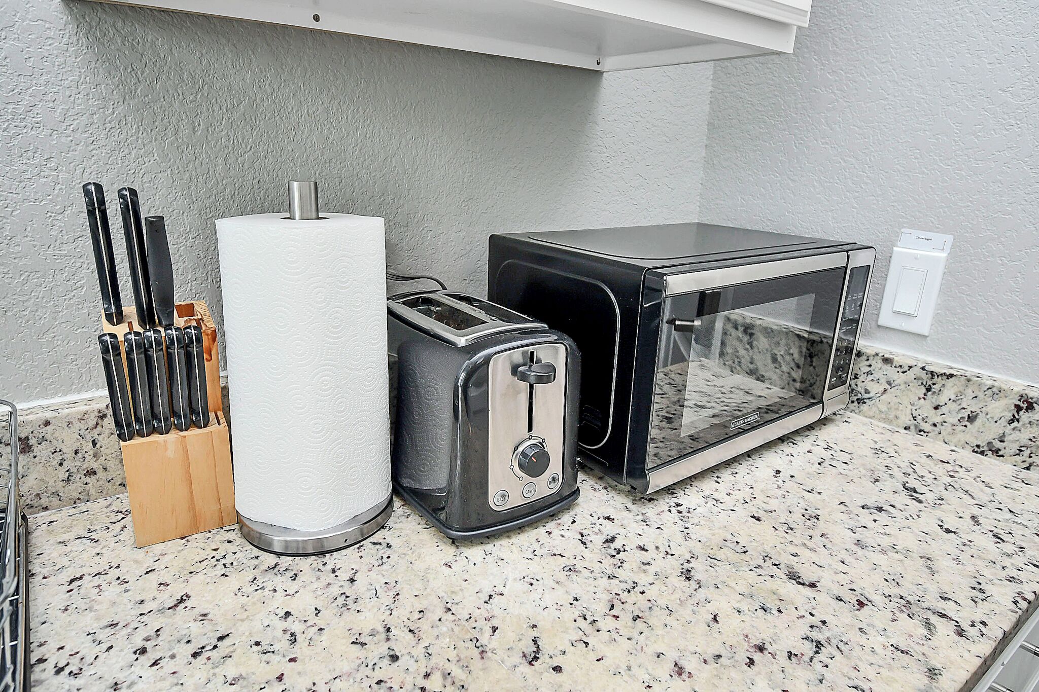 A kitchen with a granite countertop, a toaster, a microwave, and a paper towel holder.