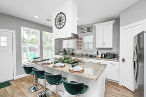 Une cuisine moderne avec un îlot central, des meubles blancs et des tabourets de bar verts.