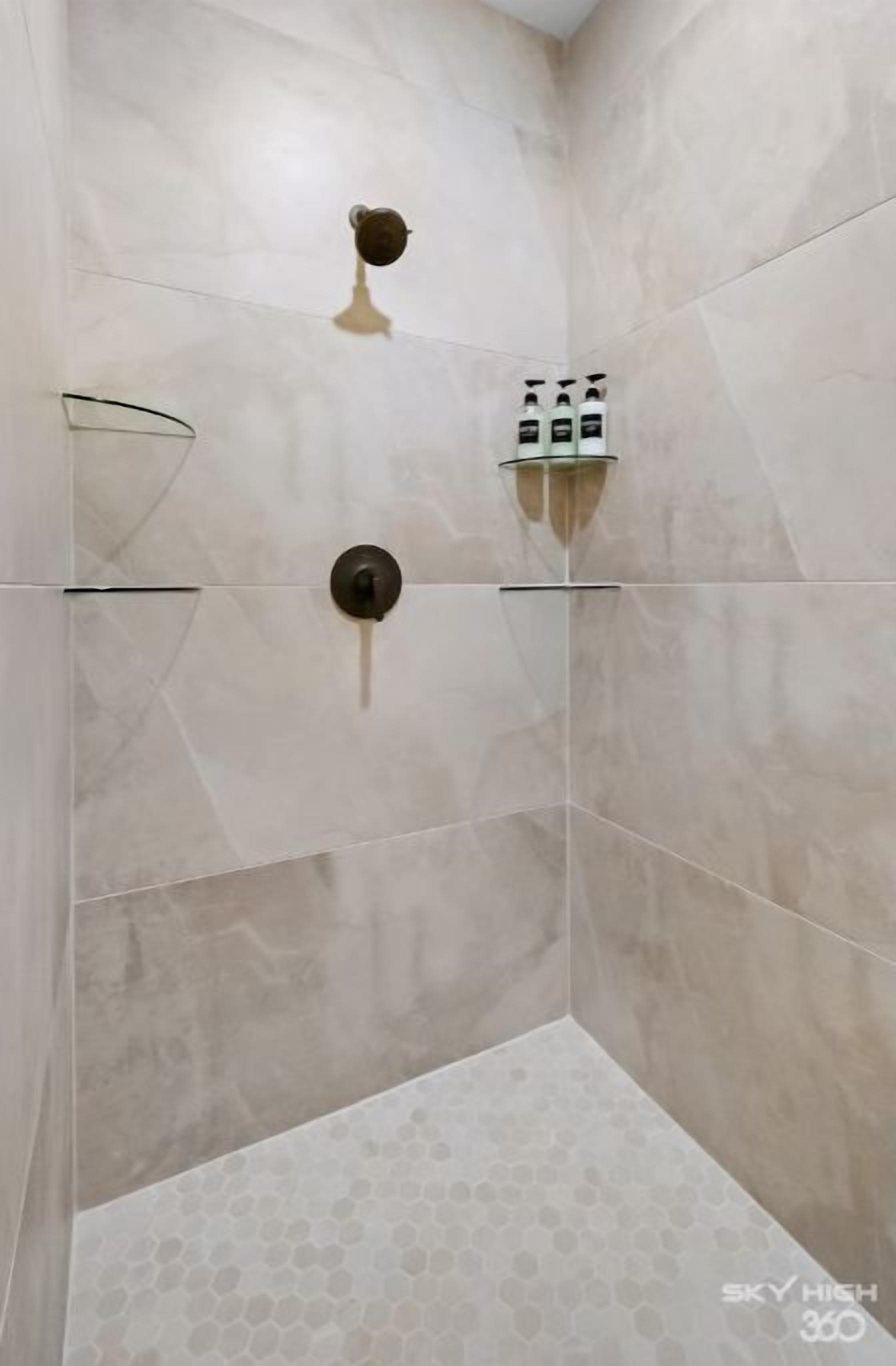 Ducha en esquina con mampara de vidrio, cabezal de ducha de mano y un juego de artículos de aseo.