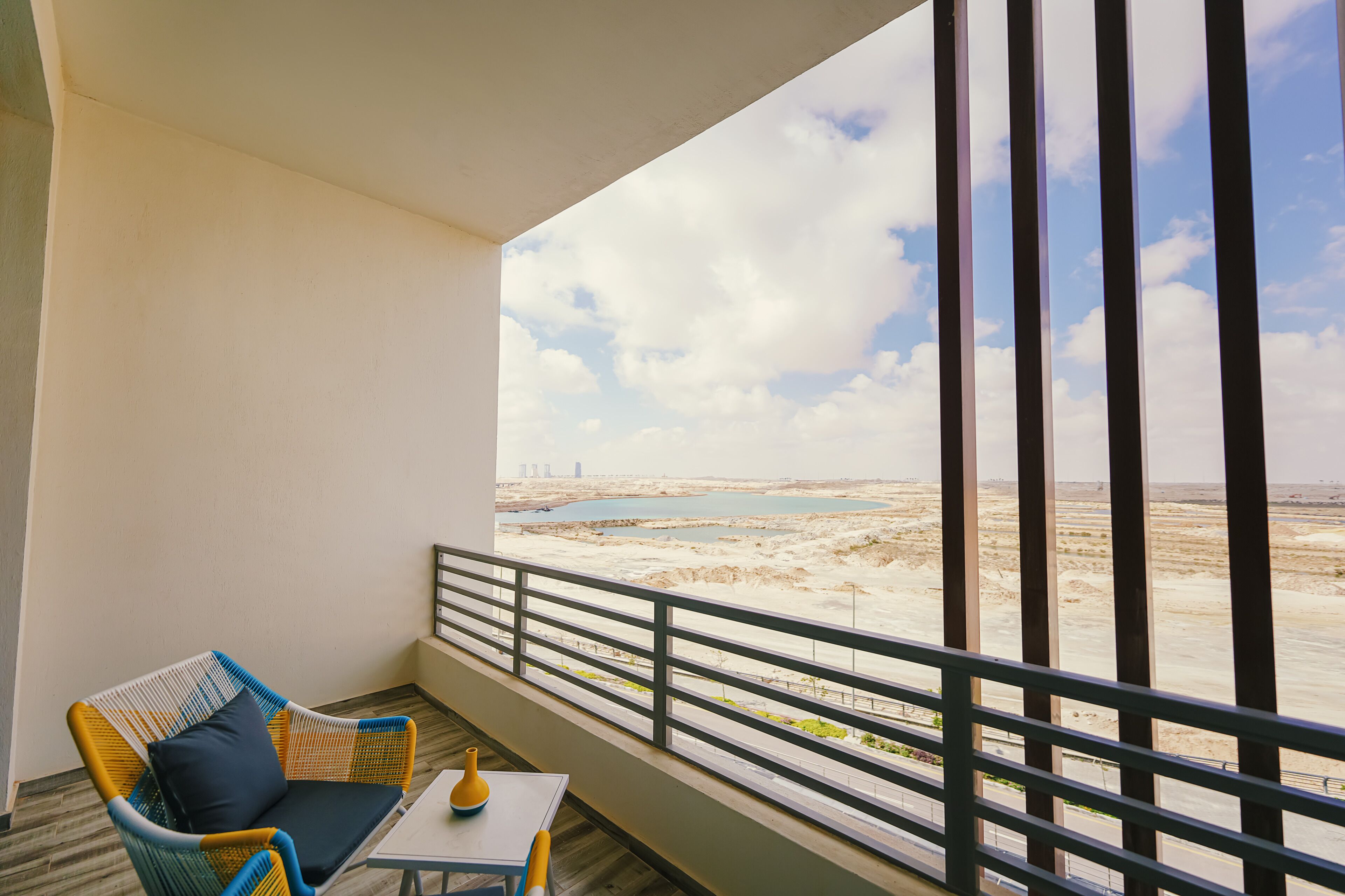 A balcony with a wicker chair, a small table, and a view of a desert landscape.