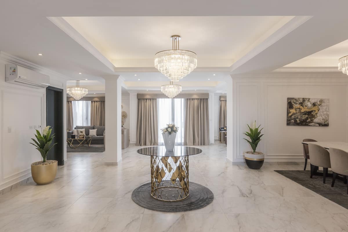 A modern dining area with a central round table, two potted plants, and a chandelier.