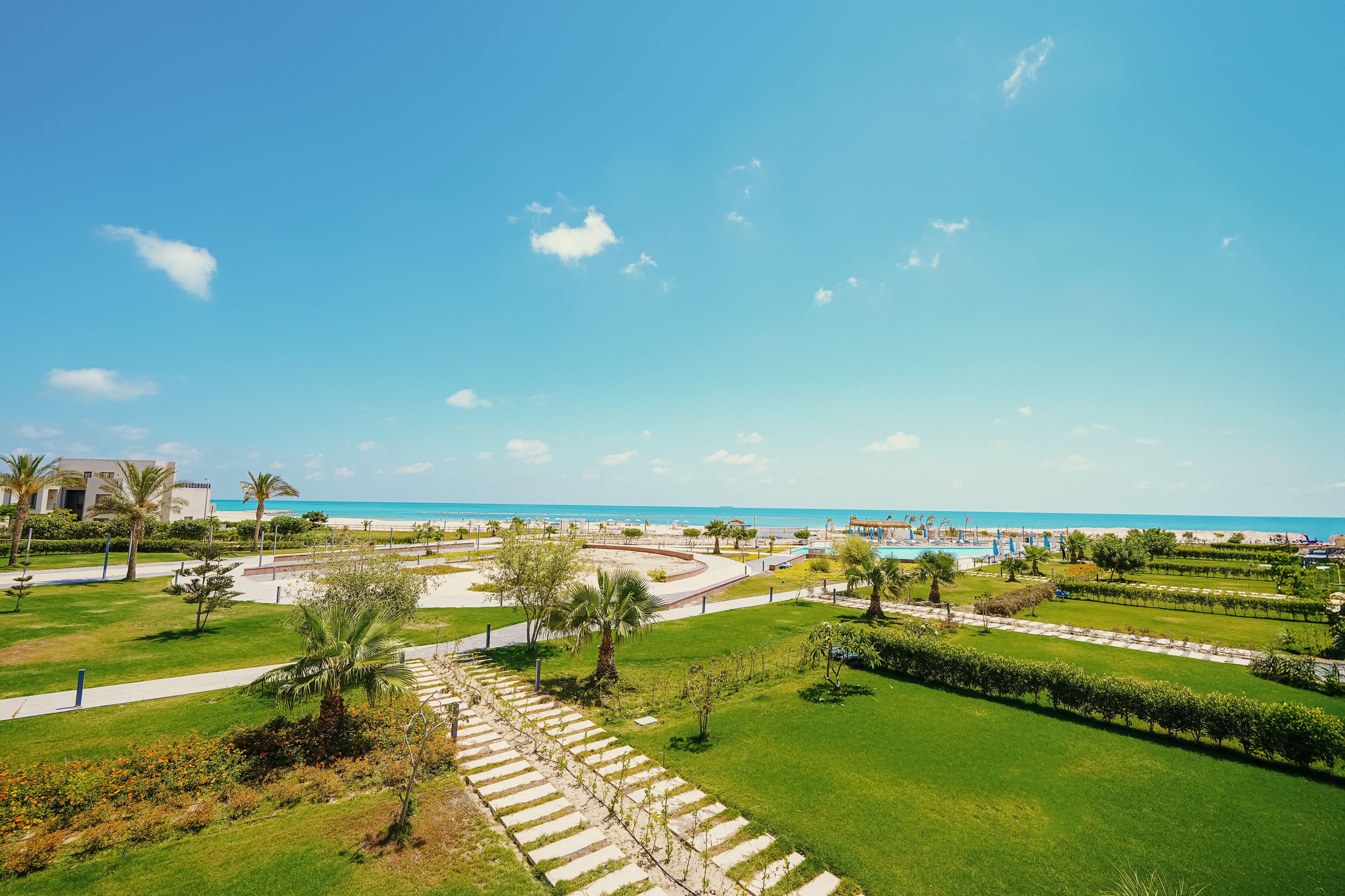 A landscaped area with pathways, palm trees, and a view of the beach and ocean.