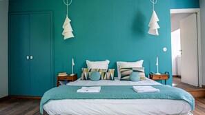 A bedroom with teal walls, a bed with white bedding, multiple pillows, two bedside tables with lamps, and a door to the left.