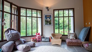 Una habitación amplia con ventanas grandes, un sillón de mimbre, un sofá y un peluche de gran tamaño.