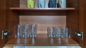 A wooden cabinet with two shelves; the top shelf holds four mugs, and the bottom shelf contains six clear glasses.