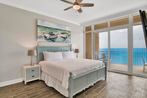 Ein Schlafzimmer mit Bett, Nachttischen, Deckenventilator, einem Gemälde von Booten und einem Balkon mit Meerblick.