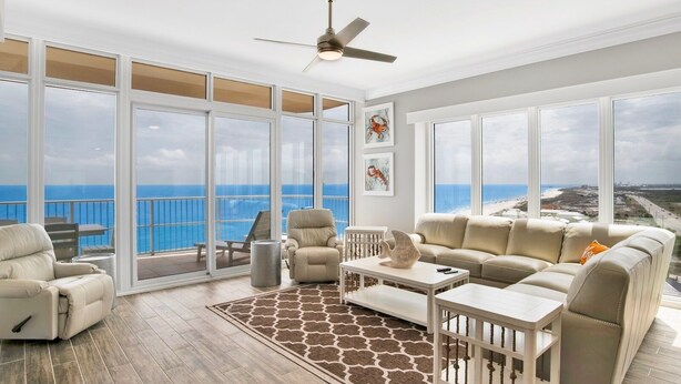 Un balcon spacieux doté de grandes fenêtres offrant une vue sur l’océan et la plage.