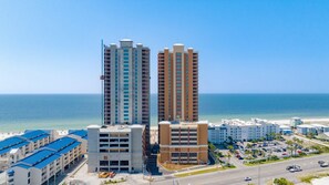 A high-rise hotel with multiple floors, a parking lot, and a view of the ocean.