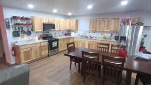 A compact kitchen with wooden cabinets, a dining table, and chairs. - Hillbilly Haven (Equinunk)