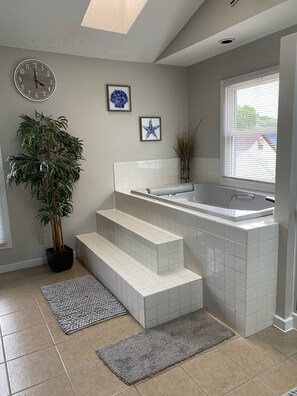 A modern bathroom with a bathtub, a potted plant, and a clock on the wall. - The Seabreeze (Dayton)