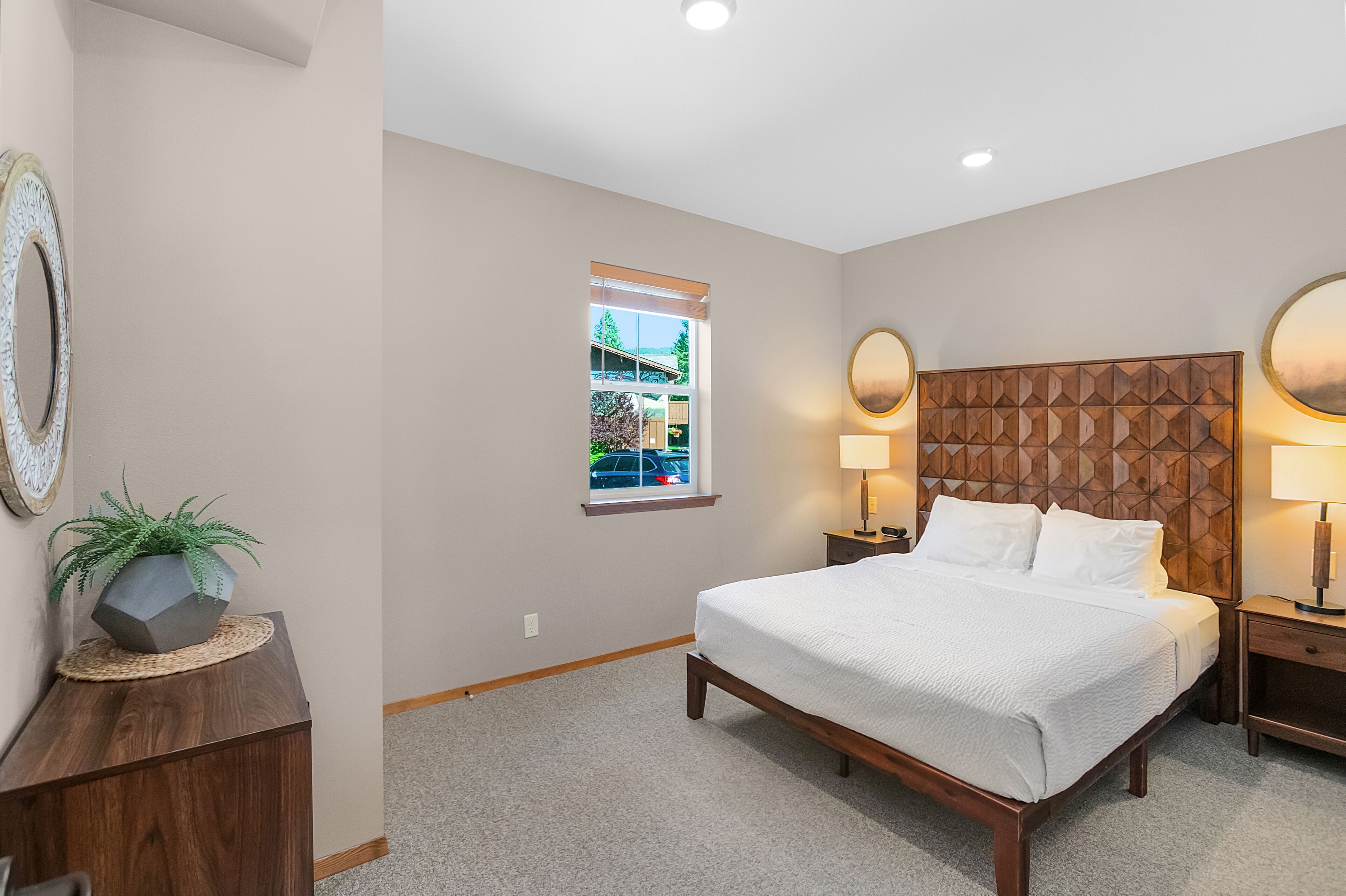 A bedroom with a bed, bedside lamps, a window with a view, and a decorative wall panel.