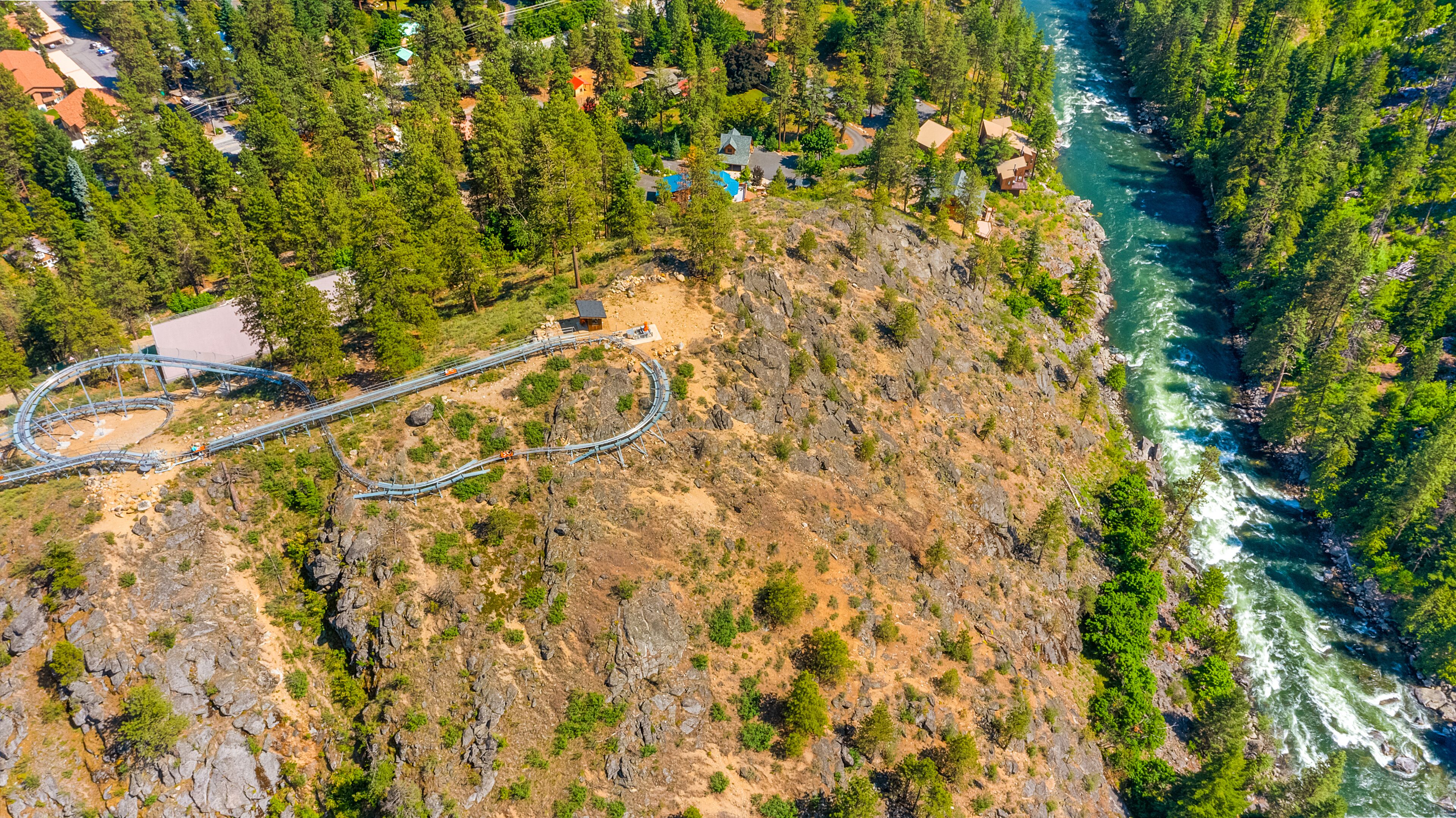 An aerial view of a mountainous area with a winding road, a small building, and a river.