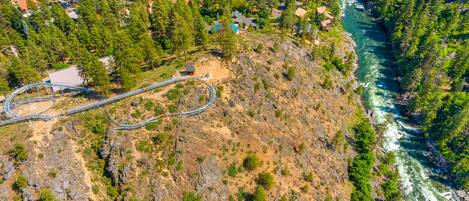 An aerial view of a mountainous area with a winding road, a small building, and a river.