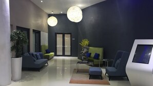 A modern lobby with a green sofa, a blue armchair, a coffee table, and a reception desk.