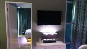 A hotel room with a flat-screen TV mounted on the wall, a bedside table with a lamp, and a bed with a headboard.