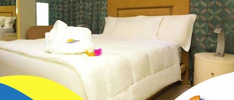 Una cama bien hecha con edredón blanco, una toalla doblada y un pequeño ramo de flores sobre la cama.