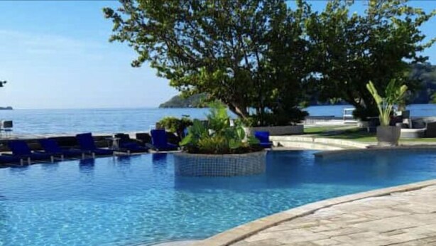 A pool with clear blue water, surrounded by stone tiles and blue lounge chairs.