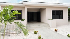 Ein modernes Haus mit Flachdach, einer Eingangstür mit Stufen und einem kleinen Garten mit Kies und Pflanzen.