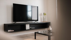 Ein modernes Wohnzimmer mit einem Flachbildfernseher an einer schwarzen Wandablage, einem kleinen Tisch mit einer Vase und einem Sessel.