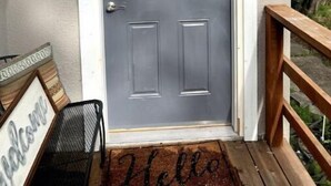 A grey door with a white frame, a metal bench, and a wooden railing. - 'Suitest' Spot Downtown. (Anchorage)