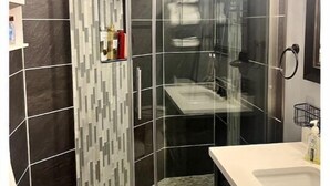 A modern bathroom with a glass shower enclosure, dark tiled walls, and a white countertop. - 'Suitest' Spot Downtown. (Anchorage)