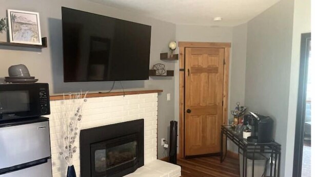 A living room with a fireplace, a television mounted above it, a microwave, and a coffee machine on a table. - 'Suitest' Spot Downtown. (Anchorage)