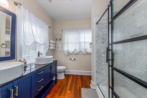 Un baño con lavamanos doble, inodoro, cabina de ducha de vidrio y suelo de madera.