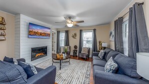 A living room with a fireplace, grey sofas, a coffee table, and a ceiling fan. - Amazing 3 BR House / Downtown New Bern / Sleeps 8 (New Bern)