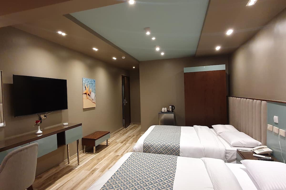Ein Hotelzimmer mit Schreibtisch, zwei Betten, einem Fernseher, einem kleinen Tisch und einer Kaffeemaschine.