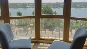 A room with two armchairs and a large window overlooking a body of water and cityscape. - Grand Bayan Hotel at Nile Plaza (Cairo)