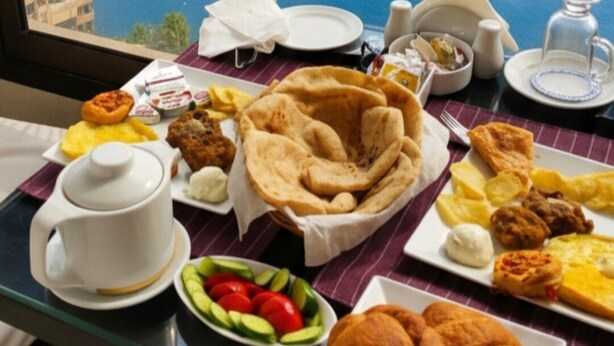 A breakfast table with various dishes, a cup, and a view of a body of water and buildings. - Grand Bayan Hotel at Nile Plaza (Cairo)