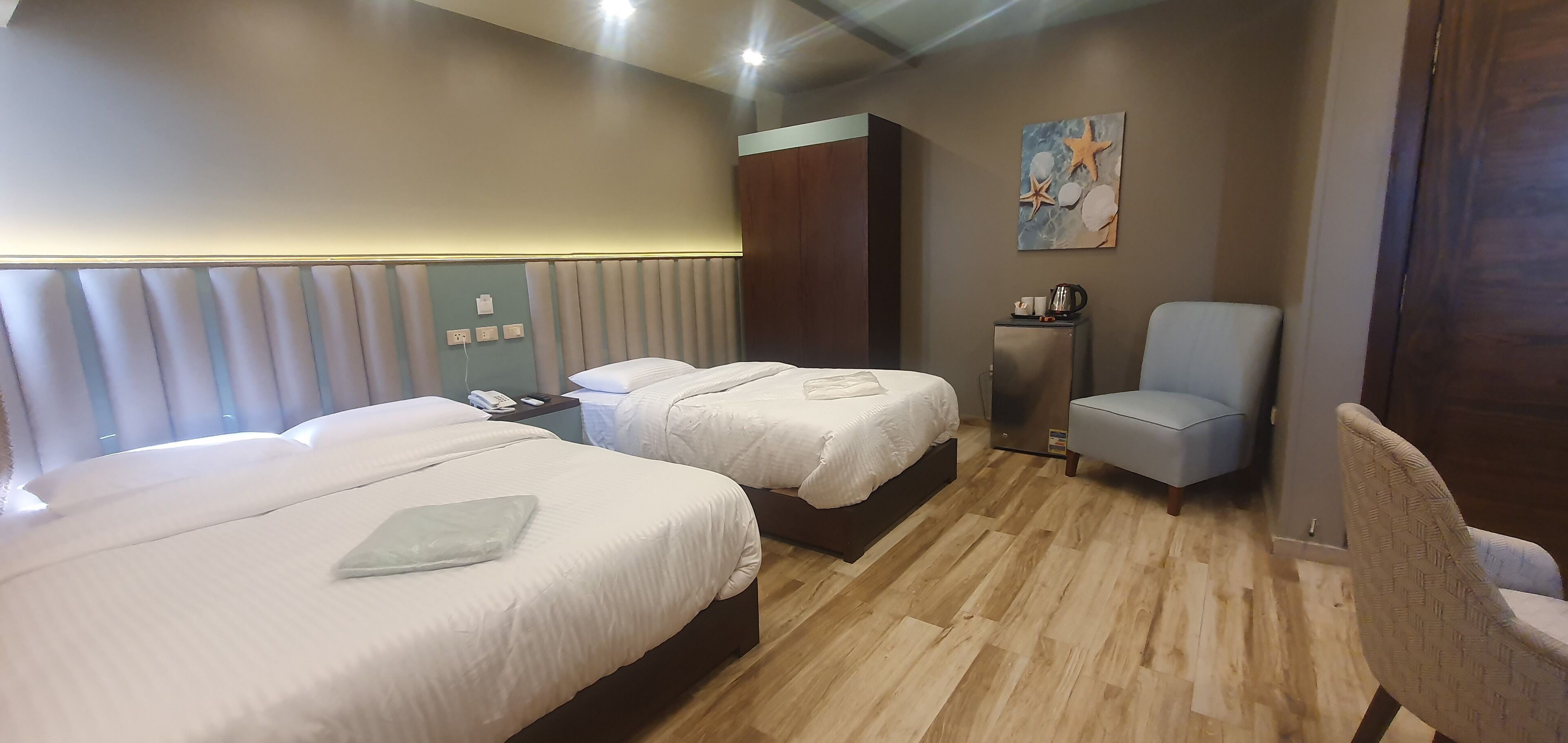 Habitación de hotel con dos camas, piso de madera, escritorio con silla, cafetera y un cuadro en la pared.