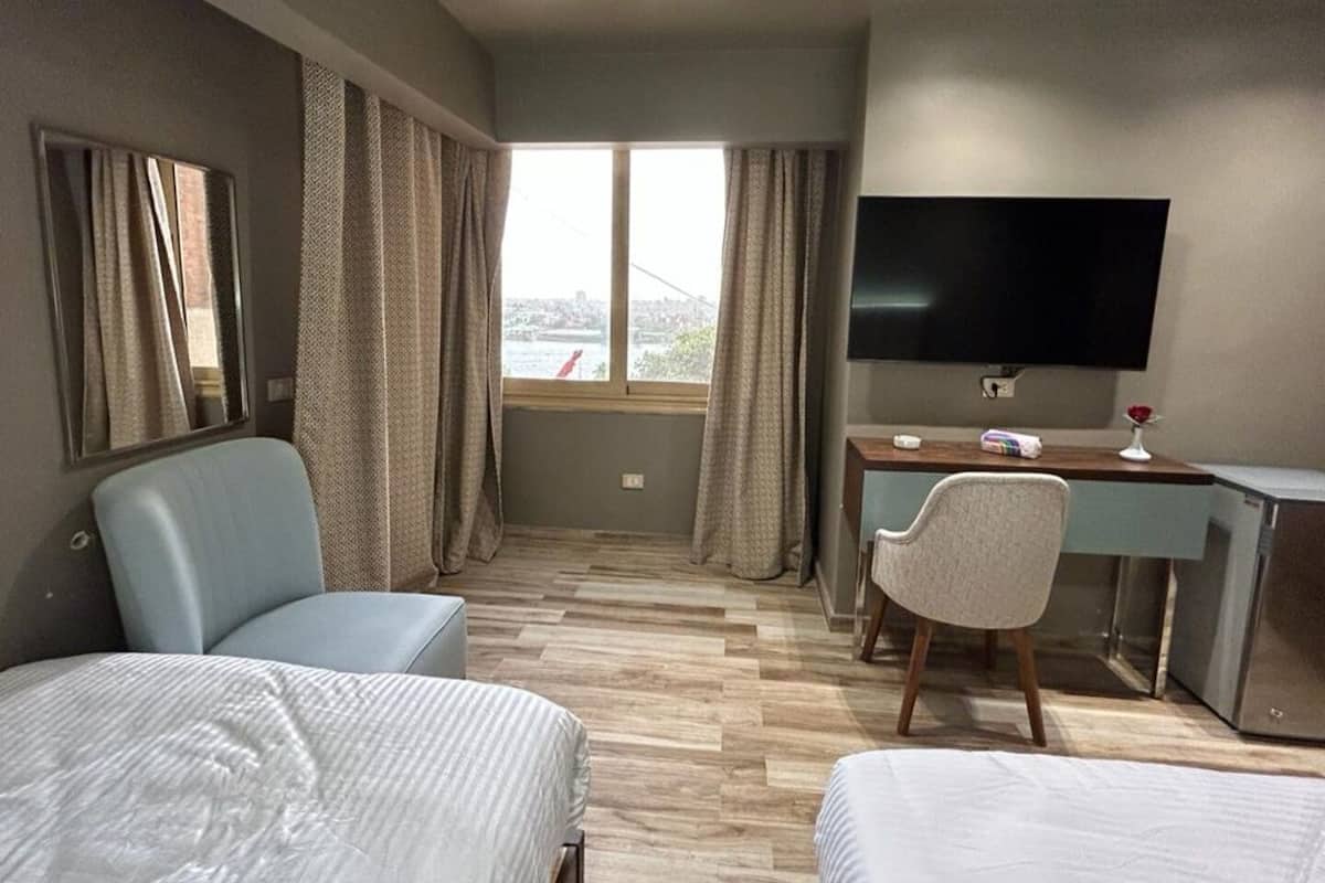 Ein Hotelzimmer mit zwei Betten, einem Schreibtisch, einem Stuhl, einem Fernseher und einem Fenster mit Vorhängen.