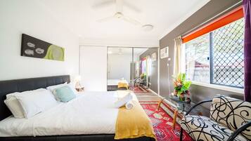 A hotel room with a bed, a ceiling fan, a window with curtains, and a view of the outside.