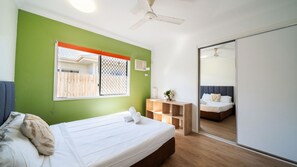 Une chambre à coucher avec un lit, une fenêtre donnant sur un beau paysage, un ventilateur de plafond et une armoire.