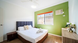 Ein Schlafzimmer mit einem Bett, Nachttischen, einem Fenster mit Ausblick und einer Wand-Klimaanlage.