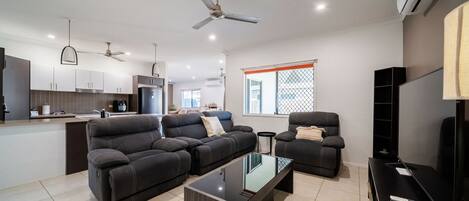 A modern living room with a sofa, armchairs, a coffee table, and a TV.