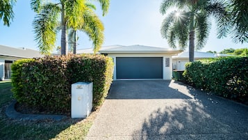 A residential property with a garage, a driveway, and surrounding greenery including palm trees and hedges.