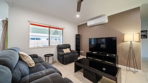 Ein modernes Wohnzimmer mit Sofa, Sessel, Fernseher und Stehlampe.