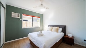 Ein Schlafzimmer mit Bett, Nachttisch, Deckenventilator, Fenster mit Aussicht und einer Wand-Klimaanlage.