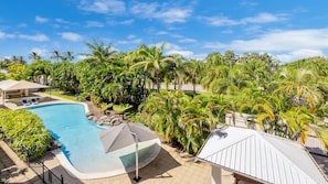 A swimming pool surrounded by lush greenery and palm trees, with a covered seating area and a white-roofed structure. - Apartment By The Harbour (Townsville)
