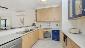 A modern kitchen with wooden cabinets, a built-in oven, a dishwasher, and a toaster. - Apartment By The Harbour (Townsville)